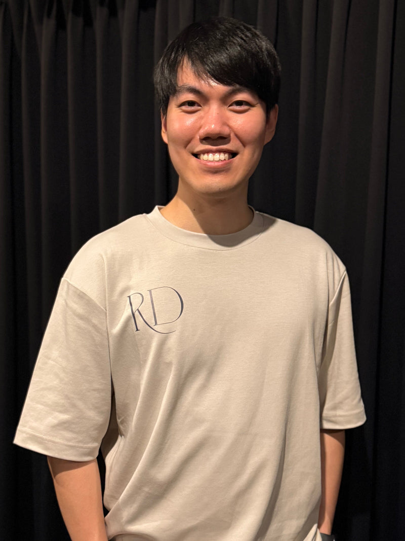 Erick Ng wearing a beige t-shirt with an RD logo against a black curtain